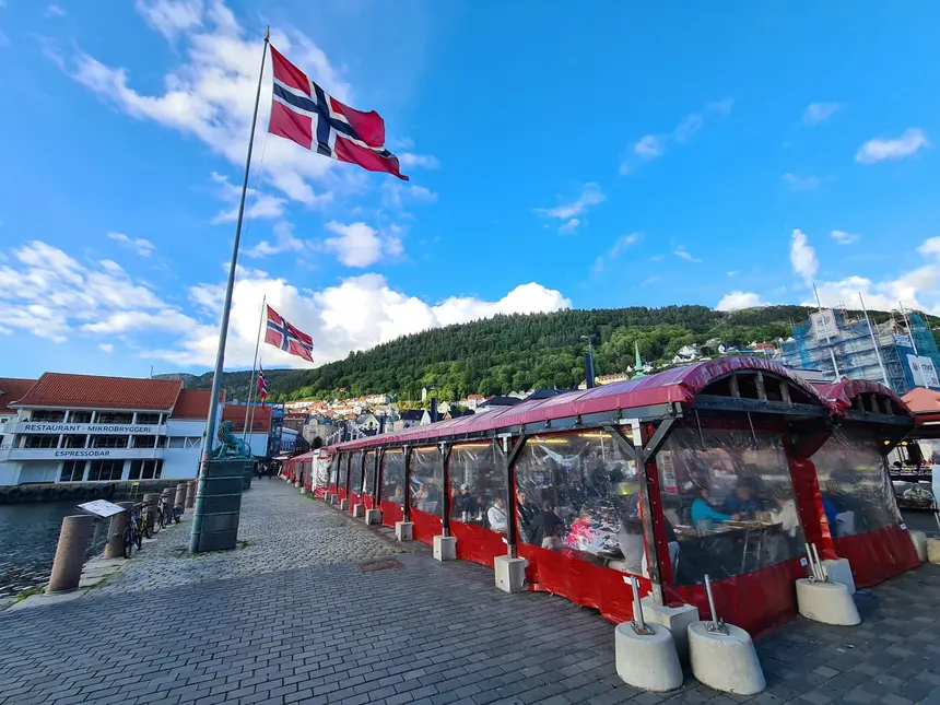 Rot überdachte Stände des Fischmarkts am Hafen von Bergen unter norwegischen Flaggen