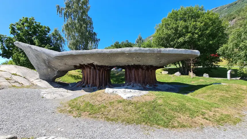 Skurriler Rastplatz-Pavillon: geschwungenes Betondach ruht auf wurzelartigen Holzstämmen