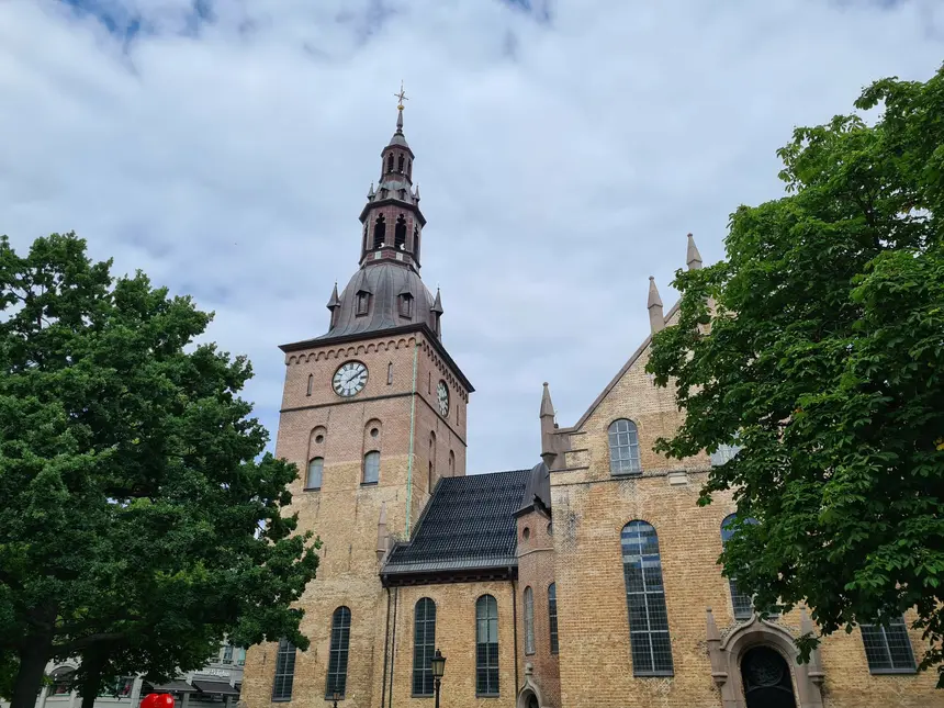 Turm der Osloer Domkirche mit Uhr und kupfergedeckter Haube hinter Bäumen
