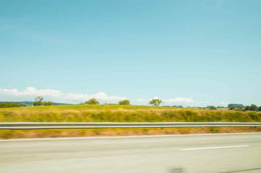 Sommerliche Felder und Leitplanke ziehen am Autofenster vorbei