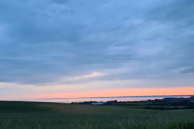 Abendrot über der Ostsee, davor Felder und ein Hof auf Møn