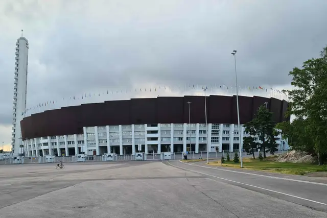 Olympiastadion Helsinki mit schlankem Turm und Fahnenkranz unter Wolkenhimmel