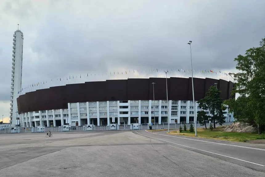 Olympiastadion Helsinki mit schlankem Turm und Fahnenkranz unter Wolkenhimmel