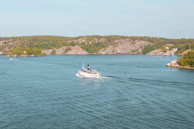 Weißes Dampferschiff zieht durch die bewaldete Schärenlandschaft vor Stockholm