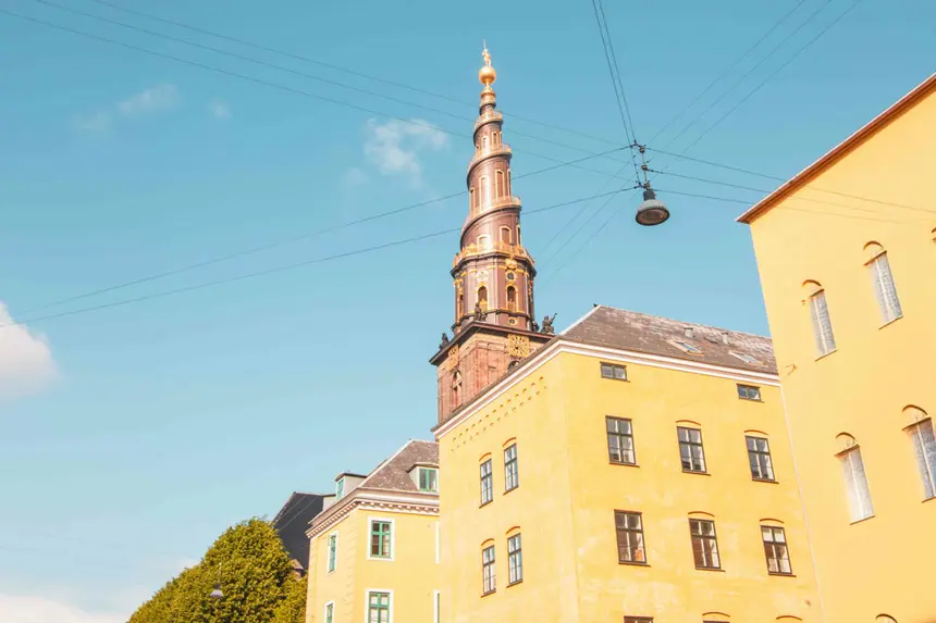 Spiralturm der Vor Frelsers Kirke mit goldener Spitze hinter gelben Altbauten in Christianshavn