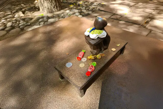 Winzige Iron-Boy-Statue mit gestrickter Mütze, umgeben von Münzen und Bonbons