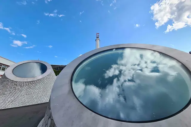 Runde Dachfenster des Amos Rex spiegeln Wolken, dahinter blauer Himmel über Helsinki