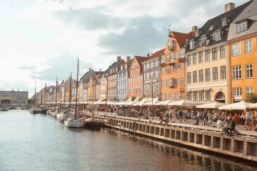 Bunte Häuserzeile am Nyhavn mit Segelbooten und belebter Uferpromenade in der Abendsonne