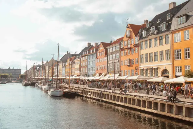 Bunte Häuserzeile am Nyhavn mit Segelbooten und belebter Uferpromenade in der Abendsonne