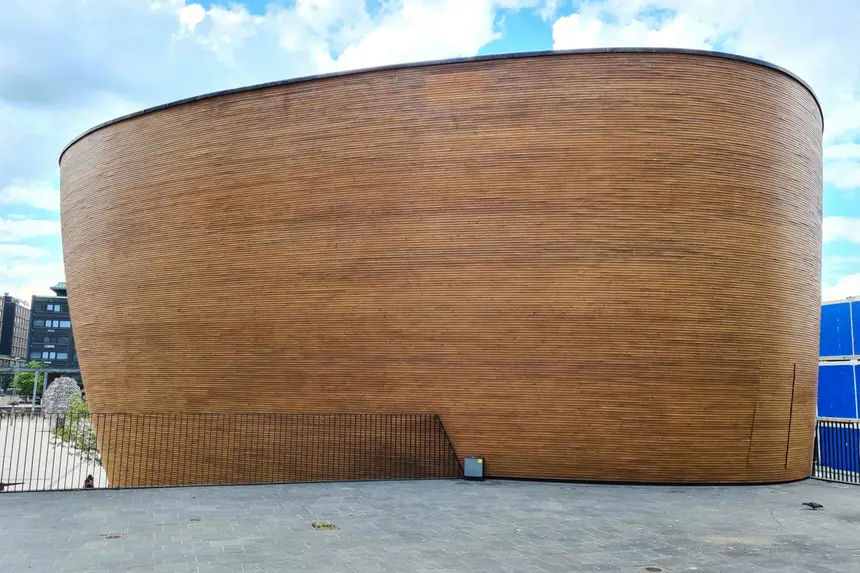 Geschwungene Holzfassade der Kampin Kappeli vor sommerlichem Wolkenhimmel
