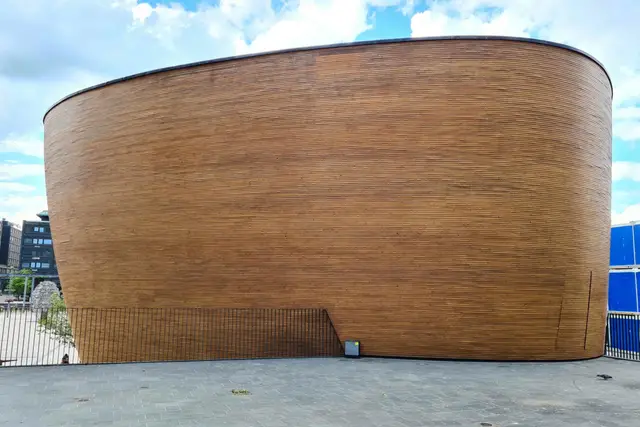 Geschwungene Holzfassade der Kampin Kappeli vor sommerlichem Wolkenhimmel