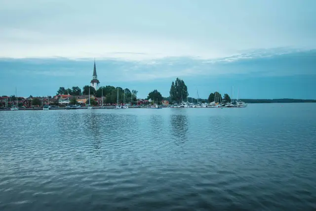 Kleiner Ort mit weißem Kirchturm und Bootsstegen am abendlich stillen Wasser