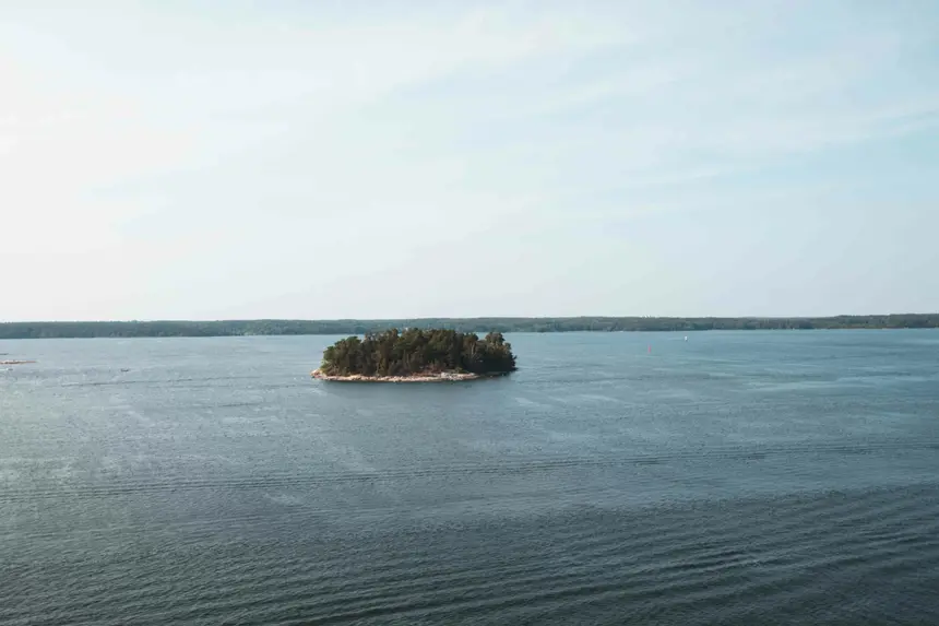 Kleine bewaldete Schäreninsel mitten im offenen Wasser, von der Fähre aus gesehen