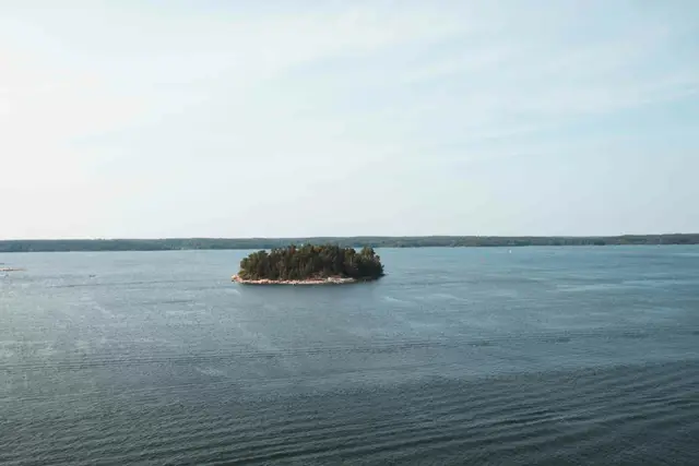 Kleine bewaldete Schäreninsel mitten im offenen Wasser, von der Fähre aus gesehen