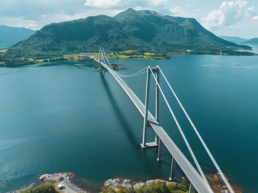 Hängebrücke spannt sich über den blauen Fjord vor bewaldetem Bergrücken