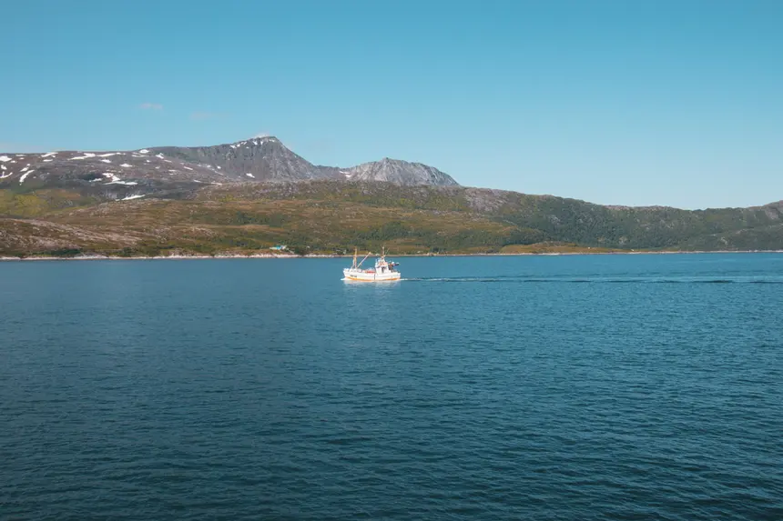 Fischkutter zieht seine Spur über das blaue Wasser vor schneegefleckten Bergen