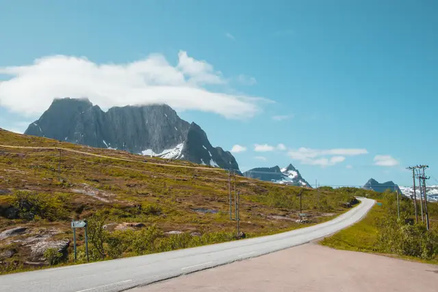 Leere Straße führt auf schroffe, wolkenverhangene Gipfel auf Senja zu