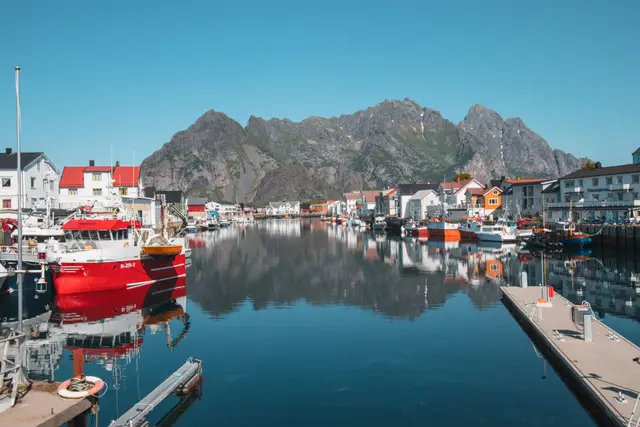 Hafenbecken von Henningsvær mit rotem Fischkutter und spiegelnden Bergen