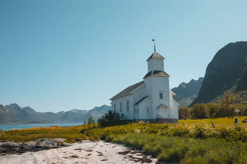 Weiße Holzkirche Gimsøy Kirke vor den Bergen der Lofoten