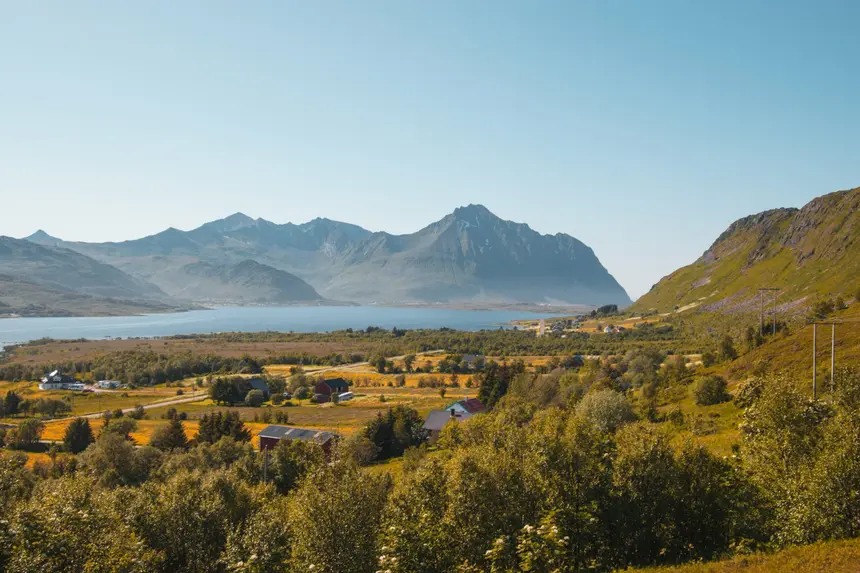 Sommerliche Lofoten-Landschaft mit Höfen, Fjord und Bergketten unter klarem Himmel