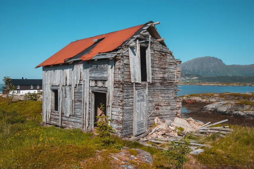 Verfallenes Holzhaus mit rostrotem Blechdach am Meer bei Borgvåg