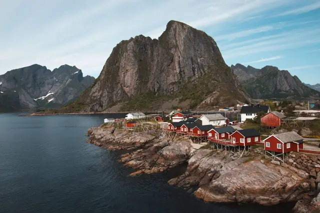 Rote Rorbuer auf Stelzen vor der steilen Bergwand von Hamnøy