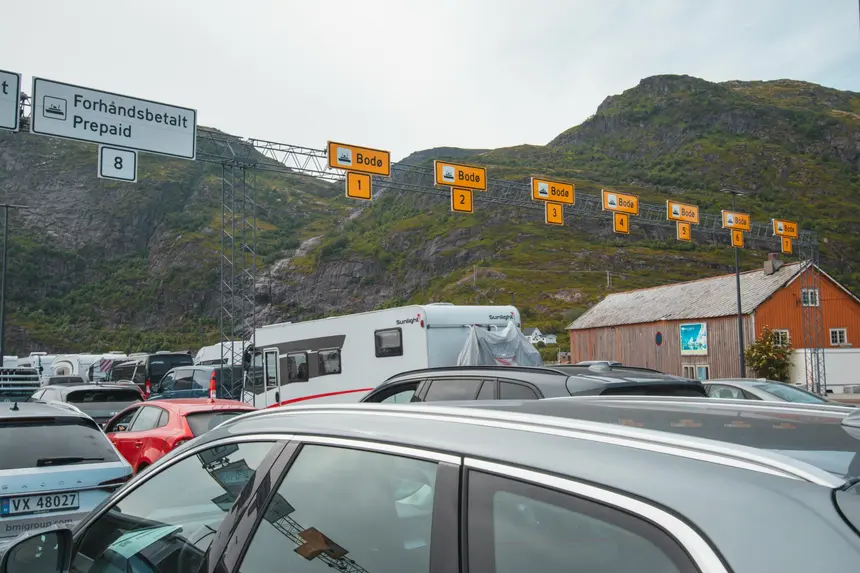 Wartende Autos unter gelben Bodø-Schildern am Fähranleger Moskenes