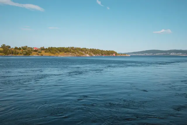 Ruhige Meerenge mit bewaldetem Ufer und rotem Bootshaus bei Bodø