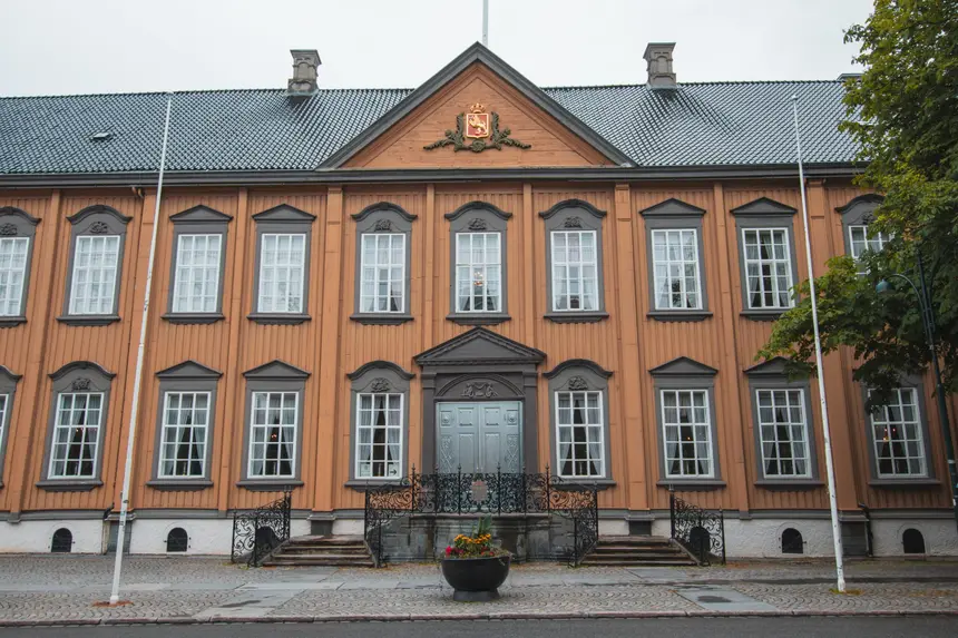 Holzfassade des Stiftsgården in Trondheim mit Wappengiebel und schmiedeeisernem Zaun