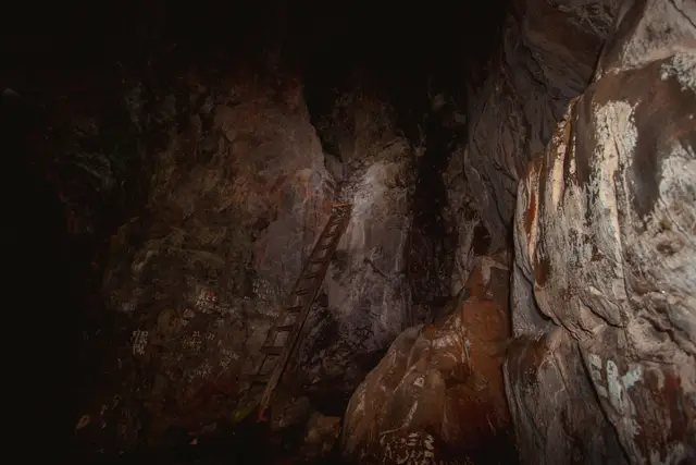 Alte Holzleiter lehnt an der Felswand einer dunklen Höhle