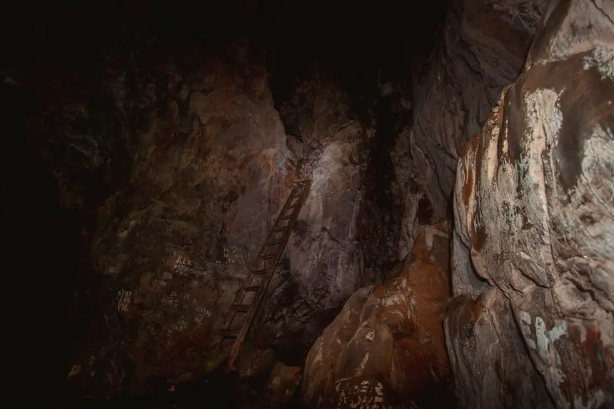Alte Holzleiter lehnt an der Felswand einer dunklen Höhle