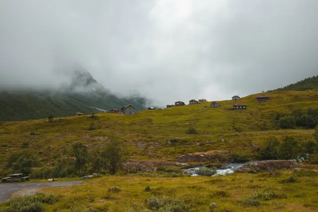 Verstreute Hütten auf grünen Almwiesen bei Byrkjelo unter tief hängenden Wolken