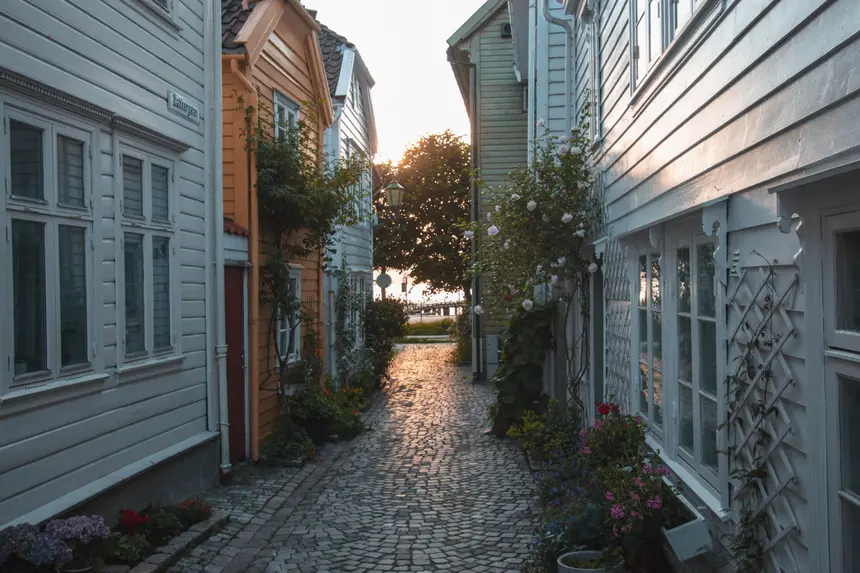 Kopfsteingepflasterte Gasse zwischen weißen Holzhäusern mit Blumen in Bergens Altstadt