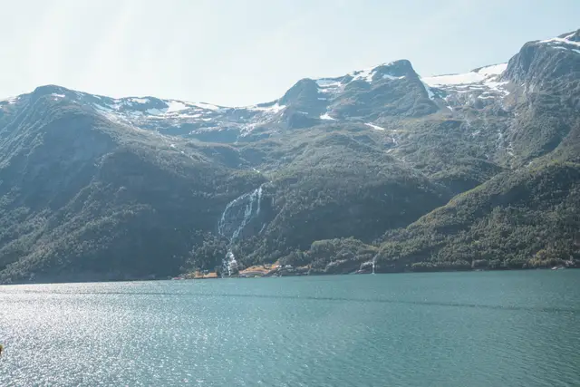 Türkisfarbener Fjord vor steilen Berghängen mit langem, dünnem Wasserfall