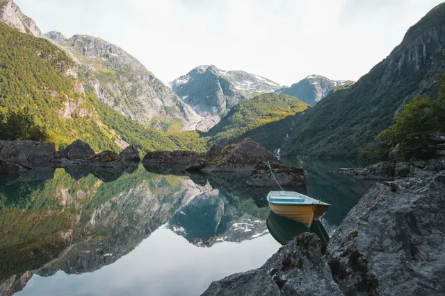 Gelbes Ruderboot auf dem spiegelglatten Bondhusvatn vor Gletscher und Bergen