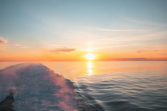 Sonnenuntergang über dem Meer mit schäumender Hecksee eines Bootes