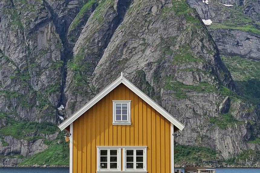Das knallgelbe Holzhaus vor der steil aufragenden Bergwand der Lofoten