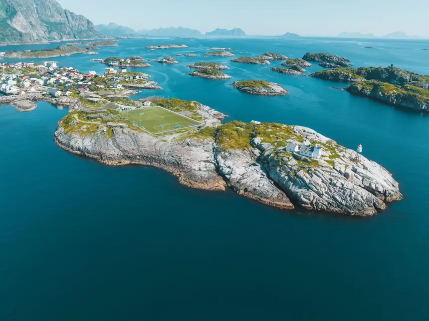 Henningsvær aus der Luft: Schäreninseln im türkisfarbenen Meer, mittendrin der berühmte Fußballplatz