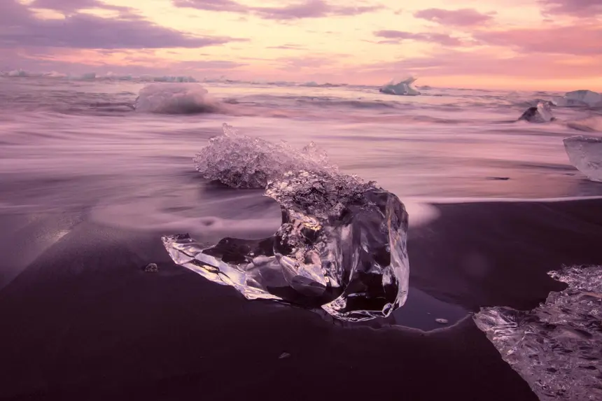 Wellen umspülen einen Eisblock am Diamond Beach