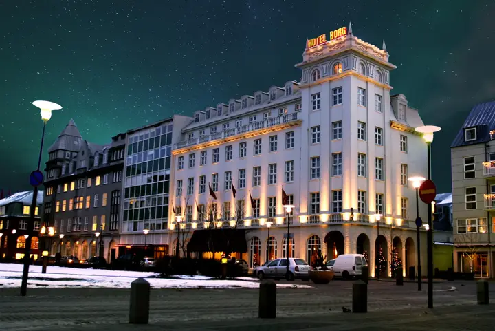 Das beleuchtete Art-déco-Gebäude des Hotel Borg am Austurvöllur in einer Winternacht mit Nordlicht