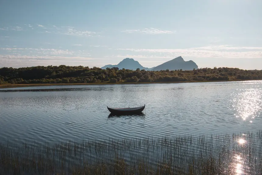 Ein einzelnes Ruderboot liegt still auf einem spiegelnden See, dahinter die Berge der Lofoten