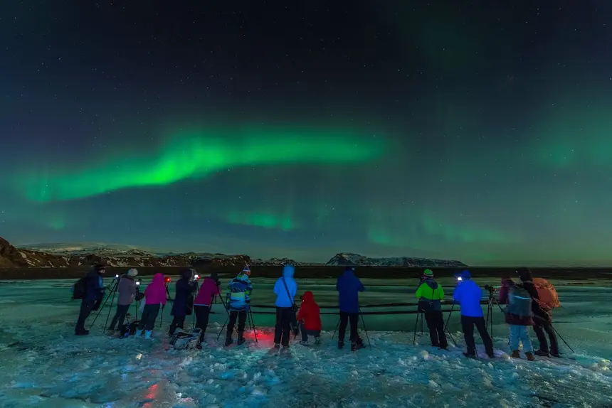 Reisegruppe beobachtet ein grünes Nordlichtband über einer Bucht