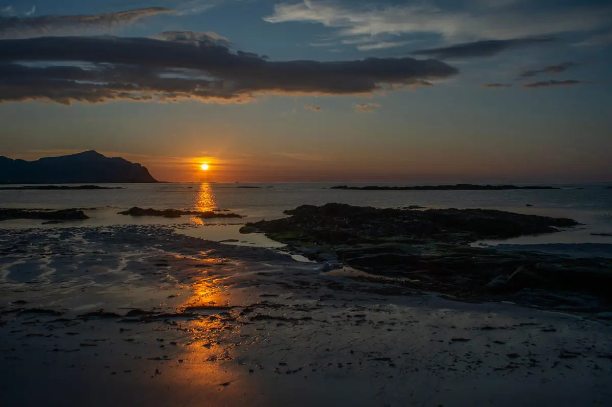 Mitternachtssonne knapp über dem Horizont an einem Strand in Nordnorwegen