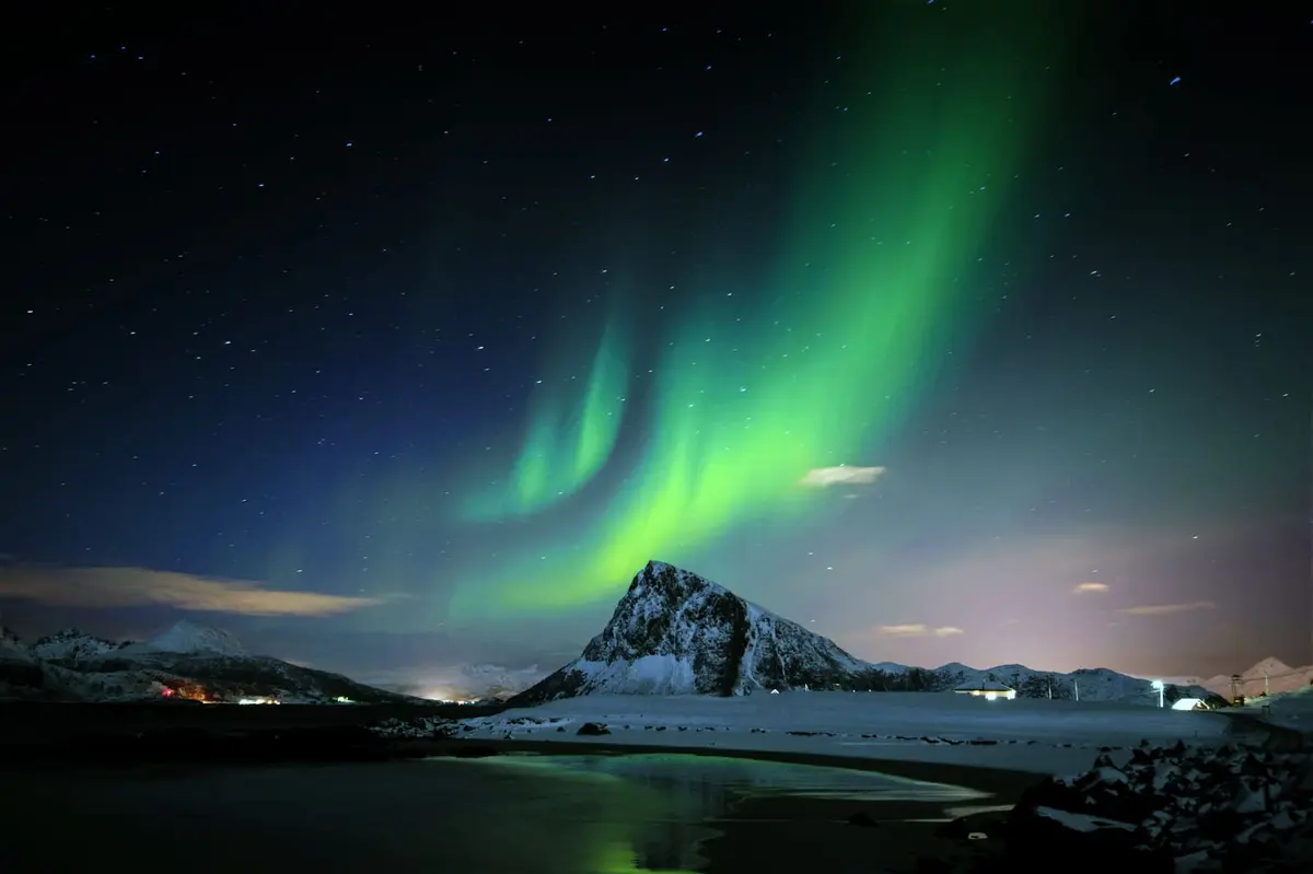 Grüne Nordlichter über einem schneebedeckten Berg an einer Bucht auf den Lofoten