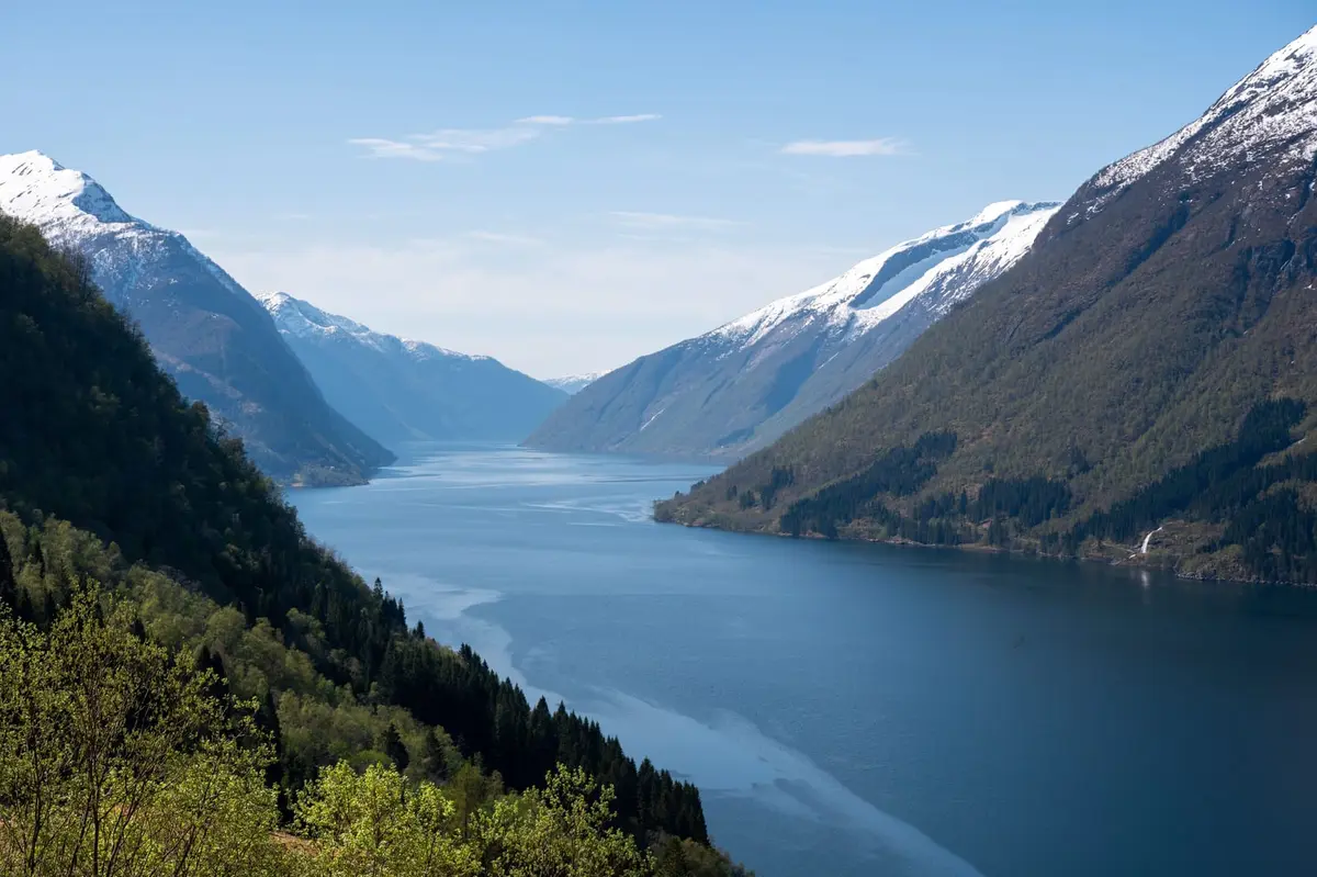 Blick von oben auf einen tiefblauen Fjord zwischen schneebedeckten Bergen in Norwegen
