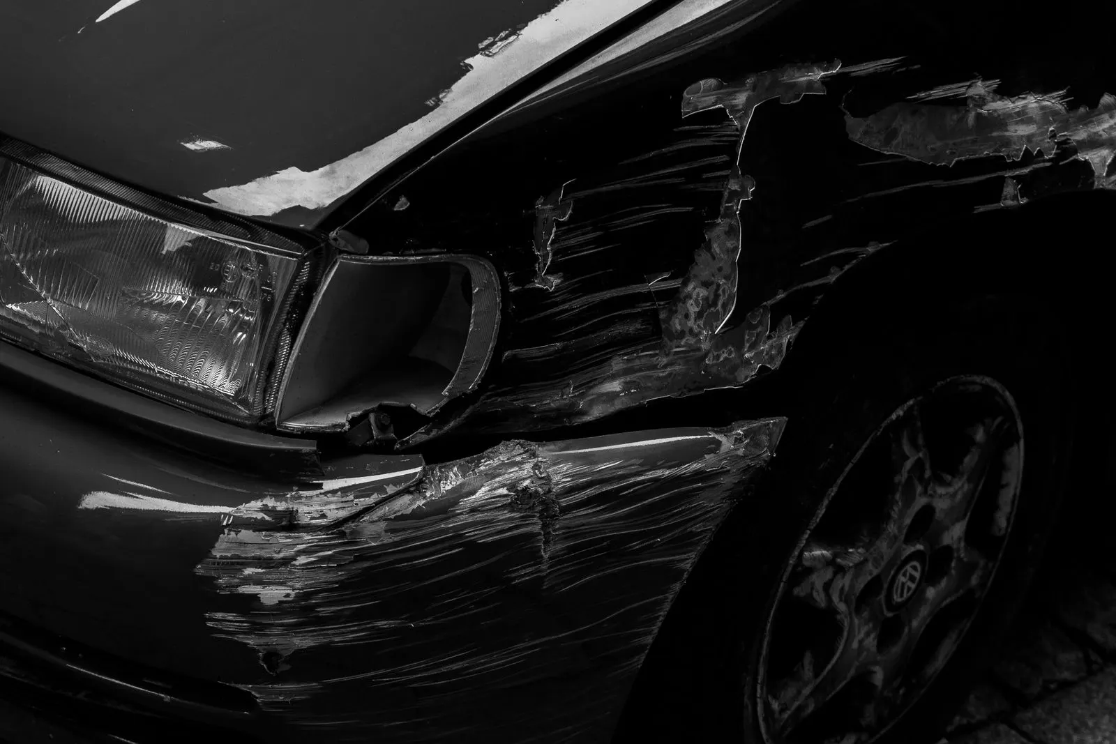 Schwarzweiß-Aufnahme einer eingedrückten und zerkratzten Fahrzeugfront nach einem Unfallschaden